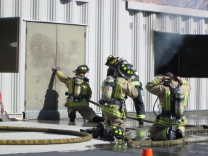 Once enough personnel was on scene, they prepare to enter the burning structure, feeling the door for heat before proceeding. Photo by Stephanie Frehner.